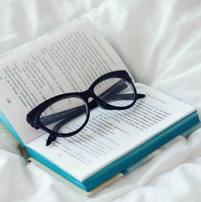 Eyeglasses placed on opened book on white bedsheets of soft bed in light bedroom